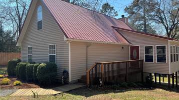 A single-story house with a red roof, a front porch with a wooden railing, and a small front yard with trimmed bushes.
