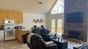A spacious living area with a stone fireplace, a kitchen with wooden cabinets, and a large window. - Lake Front Home with Fireplace Private Boat Dock & Kayaks (Milledgeville)