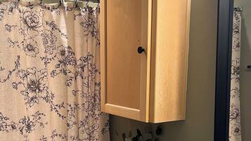 A bathroom with a toilet, a wooden cabinet, a granite countertop, a shower with a floral curtain, and a vase with a plant on the toilet.