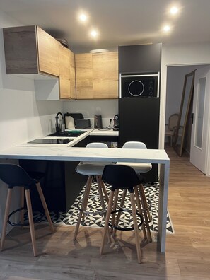 Eine kleine Küche mit weißer Arbeitsplatte, Holzschränken und einem schwarzen Kühlschrank.
