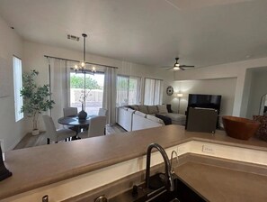 Een moderne keuken met een inbouw eiland, een eethoek met een tafel en stoelen, een bank en een televisie.