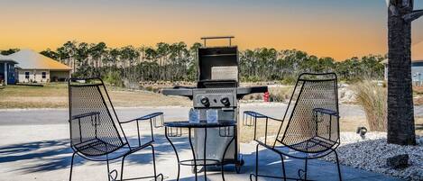 Ein Grill mit zwei Metallstühlen und einem Tisch in einer Außenanlage.