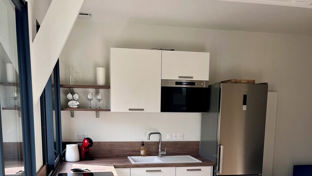 A modern kitchen with white cabinets, a stainless steel refrigerator, a microwave, and a sink. - Charming cottage (Le Mans)