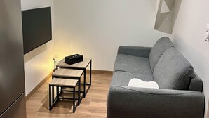 A modern living room with a grey sofa, a wooden coffee table, a flat-screen TV mounted on the wall, and a built-in bench with storage. - Charming cottage (Le Mans)