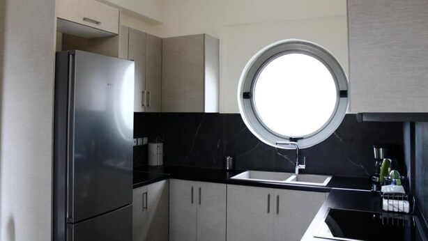 A modern kitchen with a built-in refrigerator, a round window above the sink, and light-colored cabinets.