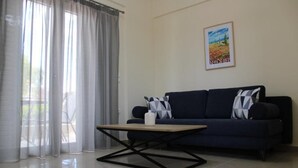 A living room with a dark blue sofa, a wooden coffee table, sheer curtains, and a framed picture on the wall.