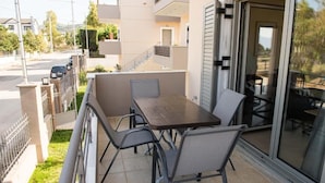 An outdoor patio with a table and chairs, a sliding glass door, and a view of the street and greenery.