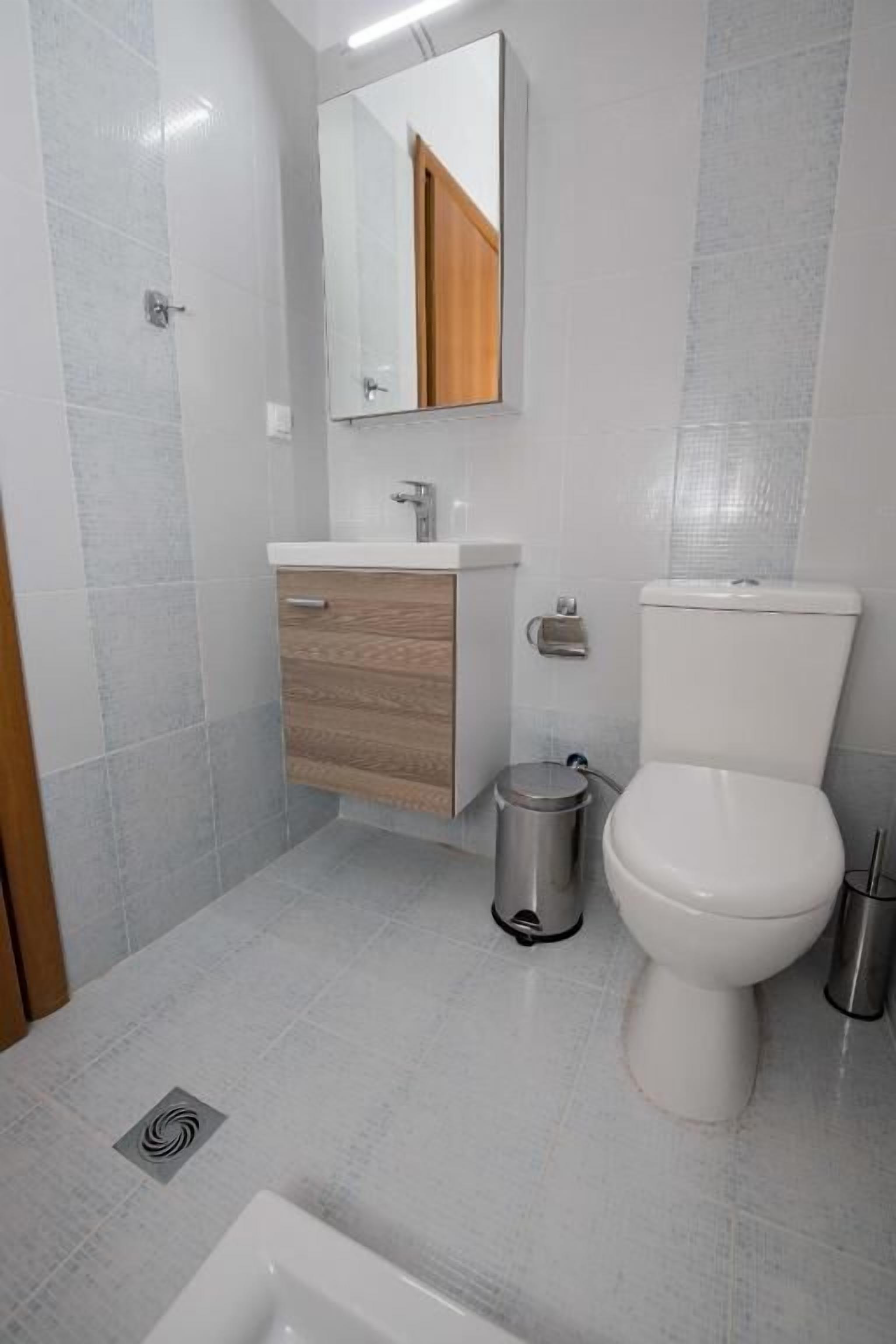 Un baño con inodoro, lavamanos, espejo y cubo de basura.