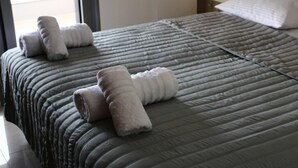 A neatly made bed with a grey quilt and two rolled towels on the side.