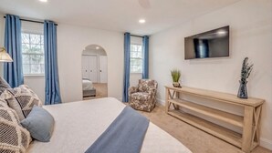 Une chambre à coucher avec un grand lit, un téléviseur fixé au mur, une chaise et une console.