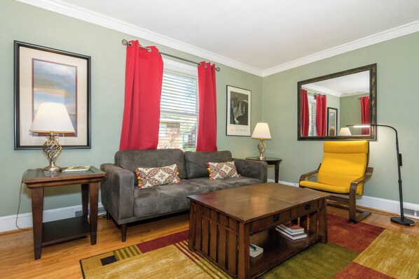 Een woonkamer met een bank, een salontafel, een gele fauteuil, een bijzettafeltje met een lamp en een grote spiegel.