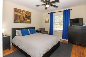 Een slaapkamer met een bed, een plafondventilator, een televisie, een dressoir en een schilderij aan de muur.