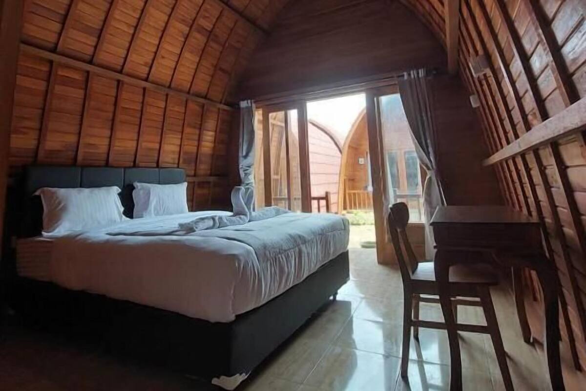 A room with a curved wooden ceiling, a bed with white bedding, a wooden table, and a chair.