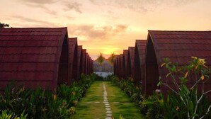 A pathway leading to a row of buildings with a sunset in the background. - les chalets pecatu (Pecatu)