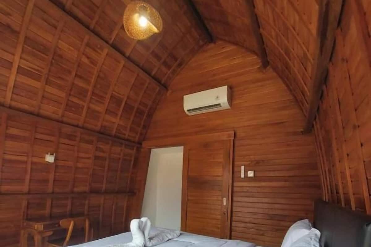 A wooden-paneled room with a bed, a desk, and a hanging light fixture.