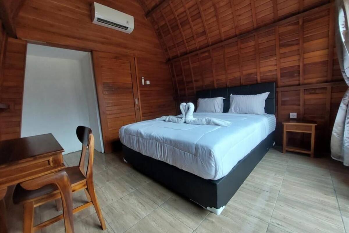 A wooden-paneled room with a bed, a desk, and an air conditioning unit.