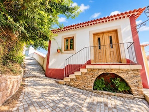 A building with a red and white facade, a stone staircase, and a small archway with greenery. - &Tales Villas Collection (Óbidos)
