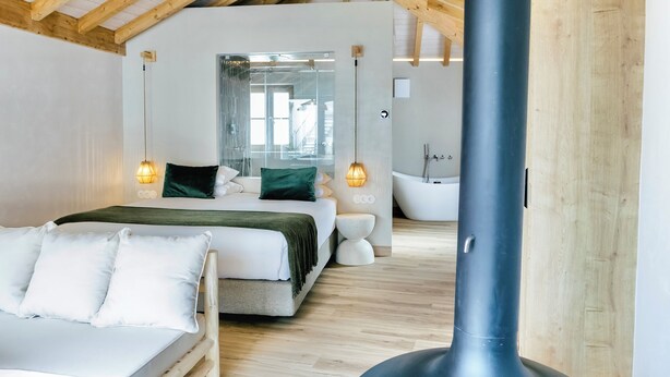 A modern bedroom with a wooden ceiling, a large bed, a separate bathroom with a bathtub, and a visible chimney. - &Tales Villas Collection (Óbidos)