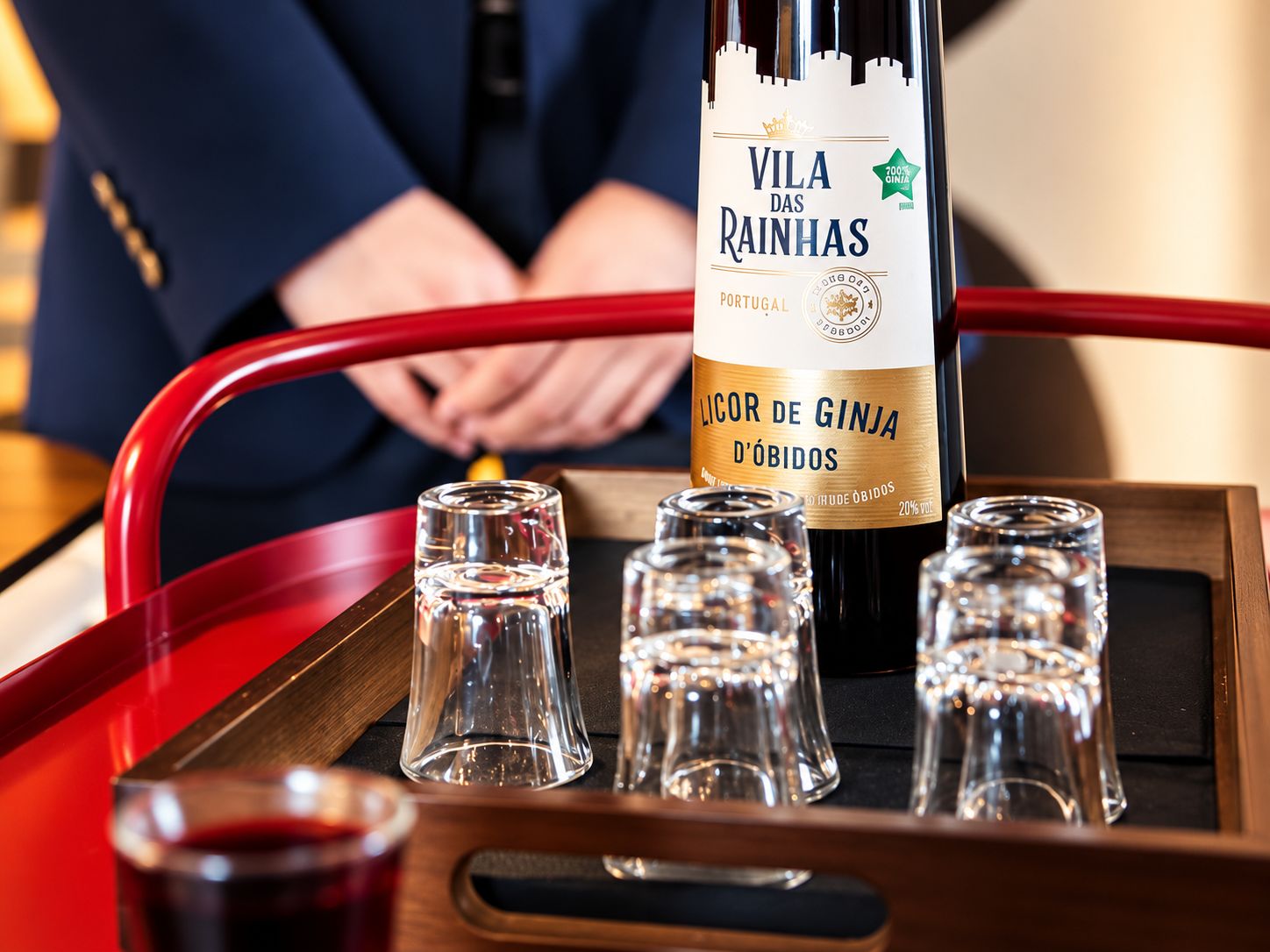 Eine Flasche Vila das Rainhas Llicor de Ginja D'Óbidos auf einem Tablett mit kleinen Gläsern.