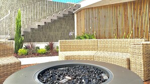 A modern outdoor seating area with wicker furniture, a fire pit, and a staircase leading to an upper level. - &Tales Villas Collection (Óbidos)