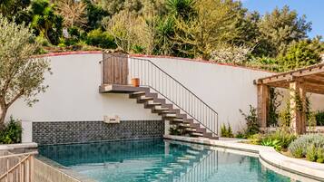 A swimming pool with a wooden deck, a staircase leading to a balcony, and a view of a castle in the background.