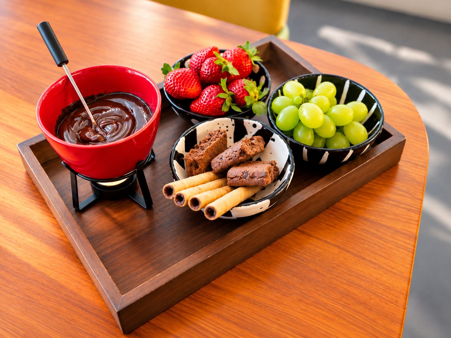 Un plateau avec un bol de chocolat fondu pour tremper les fruits, des fraises, des raisins et des biscuits enrobés de chocolat.