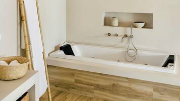 Uma casa de banho moderna com soalho de madeira, uma banheira branca, uma escada de bambu e uma prateleira com frascos e tigelas.