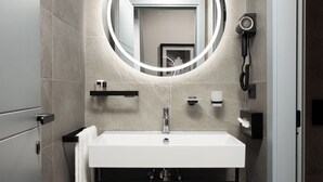 Ein modernes Badezimmer mit einem weißen Waschbecken, einem runden Spiegel mit Beleuchtung, einer Handbrause und einem Handtuchhalter.