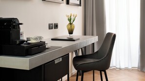 Ein modernes Hotelzimmer mit Schreibtisch, Stuhl, Kaffeemaschine und gerahmten Bildern an der Wand.