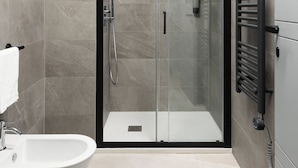Ein modernes Badezimmer mit einer begehbaren Glasdusche, einer freistehenden Badewanne und einem Handtuchhalter.