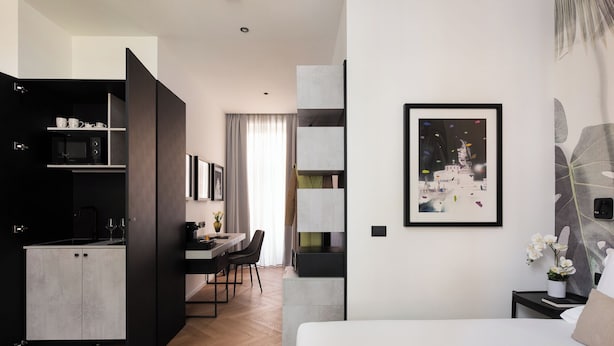 Ein modernes Hotelzimmer mit Küchenzeile, Essbereich, Bett und Kunstwerken an den Wänden.