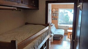 A compact room with a bunk bed, a small table, and a window providing a view of the outdoors.
