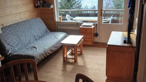 A cozy room with a sofa, a small table, a chair, a wooden cabinet, and a view through a glass door.