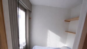 A small, narrow room with a bed, a window, and a door.
