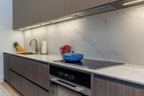 A modern kitchen with a built-in dishwasher, a stainless steel range hood, and a marble backsplash.