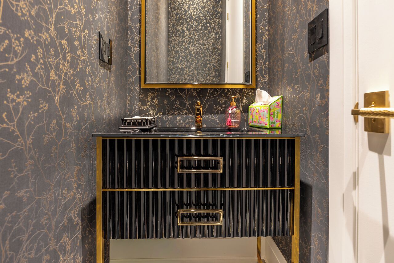 A bathroom vanity with a black and gold design, a mirror above it, and toiletries on the counter.