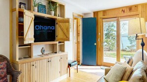 Un salon équipé d’un téléviseur, de bibliothèques en bois, d’un canapé et offrant une vue sur l’extérieur.