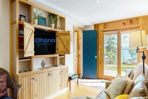 A living room with a television, wooden shelves, a sofa, and a view of the outdoors. - Mount Desert Island View (Trenton)
