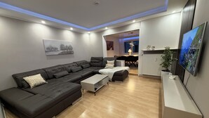 Un salon moderne avec un canapé d’angle, une table basse et un téléviseur à écran plat fixé au mur.