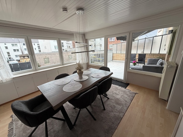 A dining area with a wooden table, black chairs, a vase, and a view of the outside.