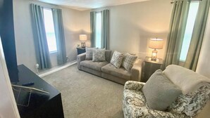 A living room with a sofa, a chair, a TV stand, and two lamps. - Cozy 1-bedroom apartment in tranquil Huntington with AC (Huntington)