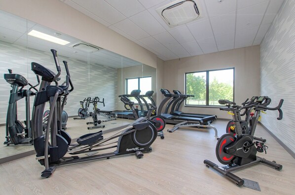 A gym with cardio machines, mirrors, and large windows.