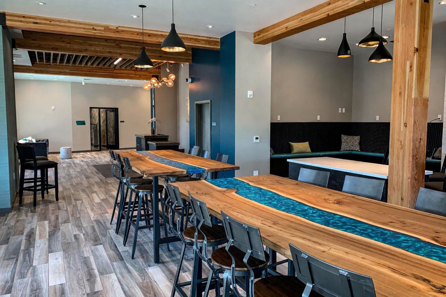 A modern bar area with wooden tables and chairs, pendant lighting, and a blue accent wall.