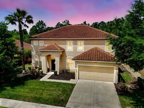 A two-story house with a tiled roof, a garage, and a well-maintained lawn. - Luxurious 5 bed Solterra Oasis close to Disney (Davenport)
