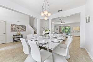 A modern dining area with a long table, white chairs, and a chandelier. - Luxurious 5 bed Solterra Oasis close to Disney (Davenport)