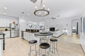 A modern kitchen with stainless steel appliances, a central island with stools, and a chandelier. - Luxurious 5 bed Solterra Oasis close to Disney (Davenport)