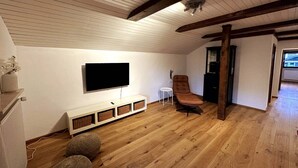 A room with a flat-screen TV mounted on the wall, a brown leather chair, a small white side table, and a wooden floor. - Vacation apartment in the Upper Bavarian Alps (Bad Kohlgrub)