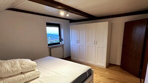 A bedroom with a bed, a window with a view, and a wardrobe. - Vacation apartment in the Upper Bavarian Alps (Bad Kohlgrub)