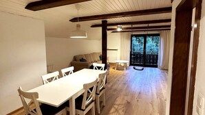 A dining area with a white table and chairs, a sofa, and a balcony with a view of trees. - Vacation apartment in the Upper Bavarian Alps (Bad Kohlgrub)