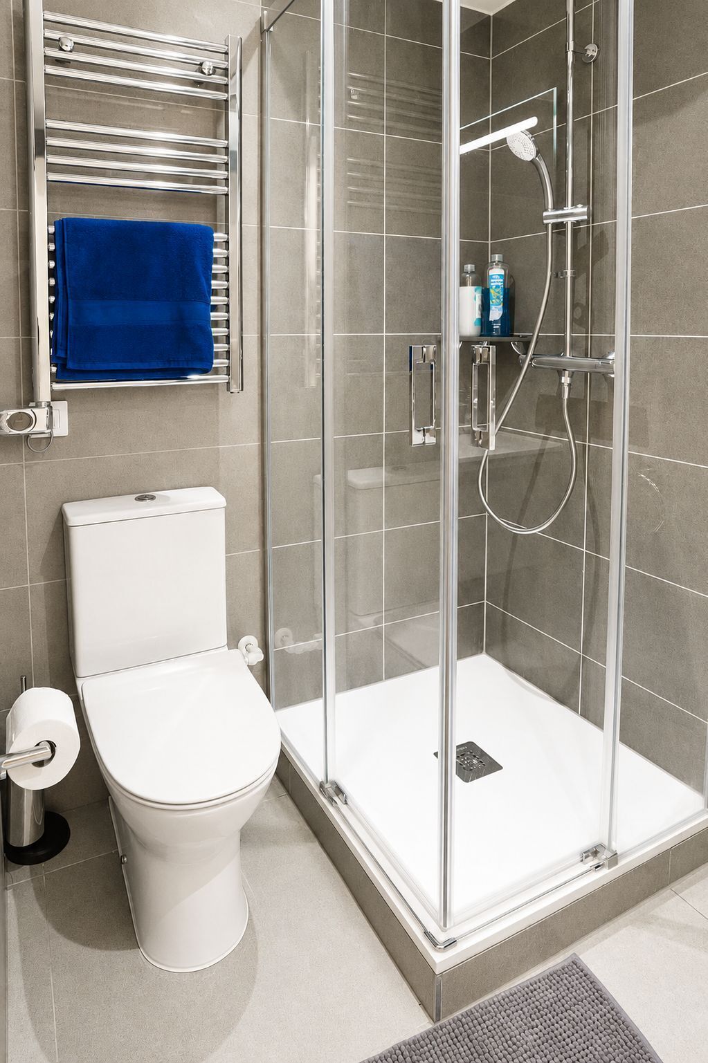 Casa de banho com sanita, cabine de duche em vidro e um porta-toalhas com uma toalha azul.